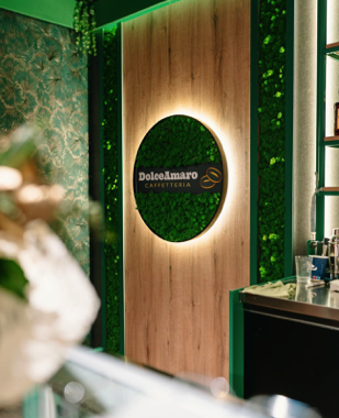 Holzwand mit beleuchtetem, rundem Moos-Logo von DolceAmaro